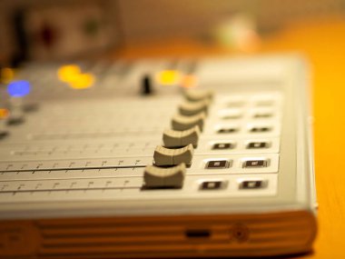 Profesyonel bir kayıt ortamında odaklanmış bir müzik prodüksiyon oturumunu gösteren çeşitli ses karıştırma konsolları ve düğmeleri belirgin bir şekilde görüntülenir.