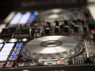 Müziği loş bir stüdyo ortamında karıştırmak için kullanılan DJ ekipmanlarının pikapları, düğmeleri ve kaydırakları gösteren yakın çekim görüntüsü. Odak noktası karmaşık detaylar..