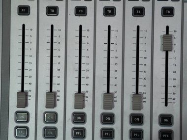 Profesyonel bir ses stüdyosunda ses karıştırmada kullanılan birden fazla sürgülü ve düğmeli bir karıştırma tahtasının detaylı bir görüntüsü. Ekipman ses mühendisliği için gereklidir..