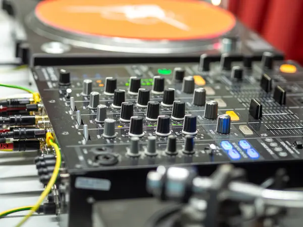 Canlı bir stüdyo ortamında çeşitli bağlantılar ve ekipmanlarla çevrili bir ses karıştırıcı konsol bulunur ve canlı bir müzik seansı için dinamik bir atmosfer yaratır..