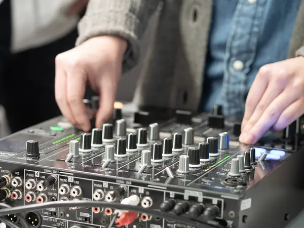 Bir DJ canlı müzik etkinliği sırasında ses mikserini ustaca yönetir. Renkli ışıklar bölgeyi aydınlatıyor, katılımcılar ritmin tadını çıkarırken enerjik titreşimleri artırıyor.
