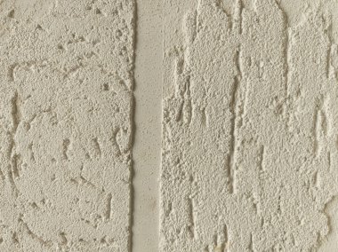 Duvarın iki bölümü farklı desenli alçı kaplamaları sergiliyor, açık nötr renkte pürüzsüz ve pürüzsüz yüzeylerin bir karışımını sergiliyor, işçilik ve tasarım sanatını ön plana çıkarıyor.