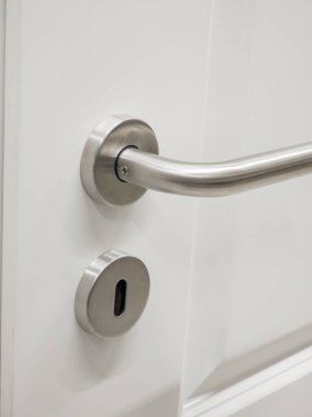 Yakın plan paslanmaz çelik bir kapı kolu ve parlak beyaz bir kapıya kilitlenerek modern minimalizmin ve modern bir ortamda fonksiyonel tasarımın altını çiziyor..