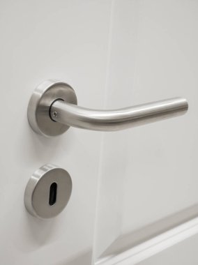 Pürüzsüz, fırçalı metal bir kapı kolunun beyaz bir kapıya dayandığı görülüyor. Bu modern tasarım herhangi bir girişe ya da iç dekorasyona zarafet katar.