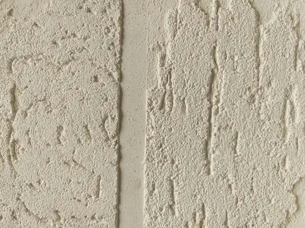 Duvarın iki bölümü farklı desenli alçı kaplamaları sergiliyor, açık nötr renkte pürüzsüz ve pürüzsüz yüzeylerin bir karışımını sergiliyor, işçilik ve tasarım sanatını ön plana çıkarıyor.