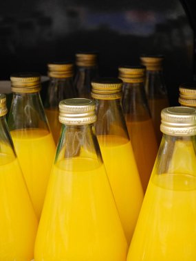 Canlı portakal suyuyla dolu cam şişeler yerel bir markette düzenlenir. Sıcak öğleden sonra güneşiyle aydınlatılır ve müşteriler ferahlatıcı bir içki içmeye davet edilir..