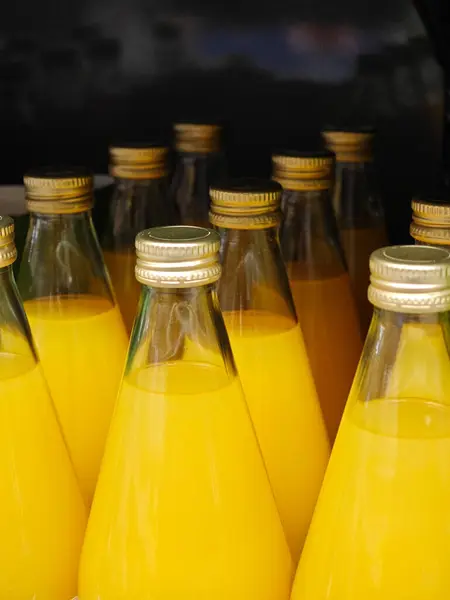 Canlı portakal suyuyla dolu cam şişeler yerel bir markette düzenlenir. Sıcak öğleden sonra güneşiyle aydınlatılır ve müşteriler ferahlatıcı bir içki içmeye davet edilir..