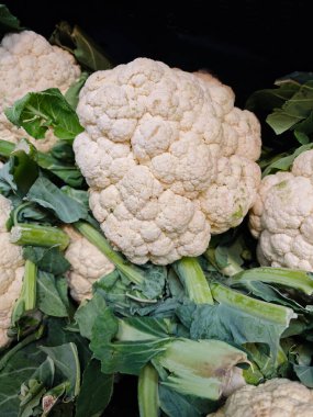 Yerel bir pazarda çeşitli taze karnabahar başları, canlı beyaz renklerini ve yeşil yapraklarını sergileyerek, ürünlerin tazeliğini ve kalitesini ön plana çıkarıyor.