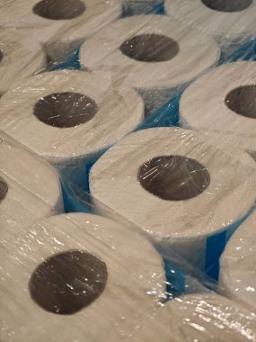 Plastiğe sıkıca sarılmış büyük miktarda tuvalet kağıdı bir depoya istiflenir. Gün ışığı filtreleri organize depolama alanını aydınlatıyor..
