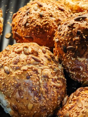 Zarif altın ekmek ruloları çeşitli tohumlarla kaplı fırın tepsisinin üzerinde oturuyor, zengin dokuları ve aromalarıyla müşterileri cezbediyor..