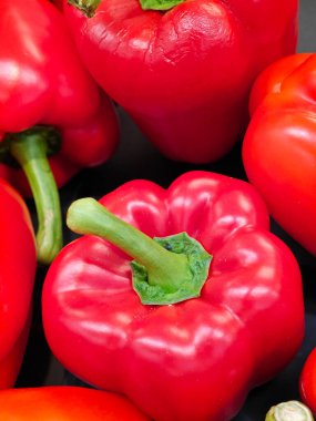 Taze kırmızı dolmalık biberlerin yakın plan görüntüsü parlak ciltlerini ve zengin renklerini ön plana çıkarıyor. Biberler bir araya getirilmiş, benzersiz şekillerini ve dokularını koyu bir arka planda sergiliyorlar..