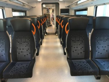 Modern bir trenin iç kısımlarında, ergonomik dizaynlı ve şık koltuklar sergileniyor. Gündüz varış yerleri arasında seyahat eden yolcular için temiz ve ferah bir ortam sunuyor..