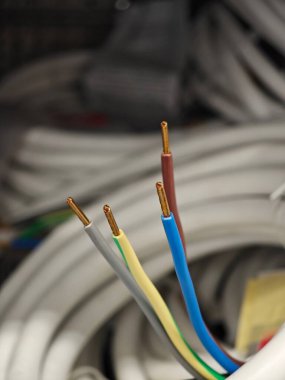 Renk kodlu elektrik kabloları çalışma alanındaki sarmalanmış kablolar arasında gösteriliyor, öğleden sonra bir inşaat projesi sırasında bir binaya yerleştirilmeye hazır..