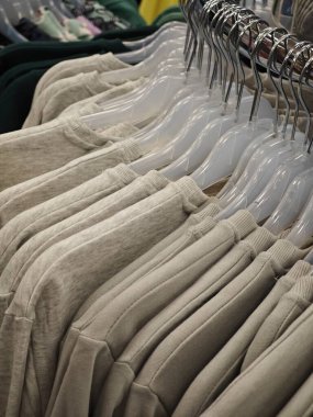 Bir perakende giyim mağazasında bej kazaklar temiz plastik askılarda sergilenir. Yumuşak kumaşlar ve düzenli düzenlemeler davetkar bir alışveriş ortamı yaratır..