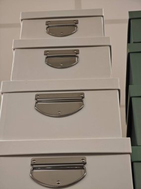 Pürüzsüz, açık renkli yüzeyleri ve parlak metal sapları olan dört depolama kutusu dikey bir yığın halinde düzenlenmiştir. Arka plan, kapalı bir ortamın düzenli olduğunu gösteriyor..