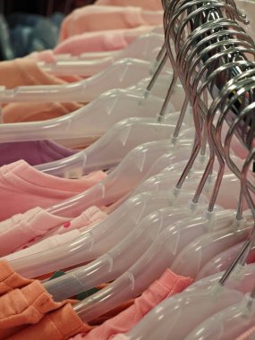 Pembe ve turuncu tonlarda çeşitli pastel gömlekler bir giyim mağazasında açık plastik askılara yerleştirilerek müşterileri bahar kıyafetleri için gezmeye ve alışverişe davet edilir..