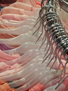 Parlak renkli giysi ürünleri bir perakende mağazasındaki temiz plastik askılara düzgünce yerleştirilmiştir. Düzenleme çeşitli tonlar ve stiller için görsel olarak çekici bir görüntü oluşturur.