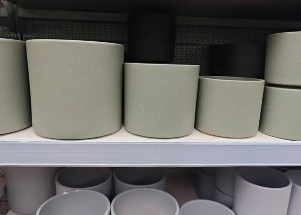 Seramik tencereler farklı boyutlarda ve şekillerde mağaza raflarında düzgün bir şekilde dizilmiş. Tencereler açık yeşil bir kaplama içeriyor, herhangi bir dekora modern bir dokunuş ekliyor..