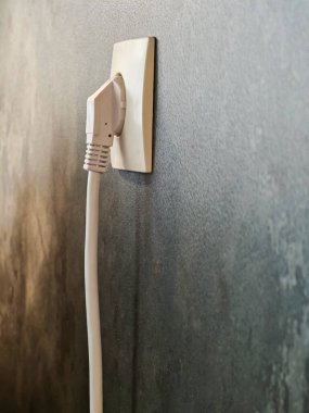 Beyaz bir elektrik prizine yakın plan. Duvara bağlı gri arka plan, enerji erişimini ve modern elektrikli aletleri sembolize ediyor..