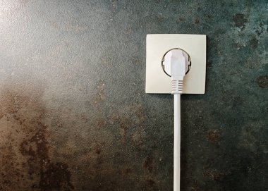 Beyaz bir elektrik prizine yakın plan. Duvara bağlı gri arka plan, enerji erişimini ve modern elektrikli aletleri sembolize ediyor..
