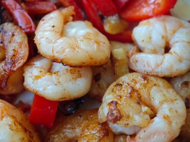 Lezzetli karidesler, canlı kırmızı dolmalık biberlerle birlikte mükemmel bir şekilde pişirilir. Bir ev mutfağında, sıcak öğleden sonra ışığıyla aydınlatılan enfes bir yemek anı sergilerler..