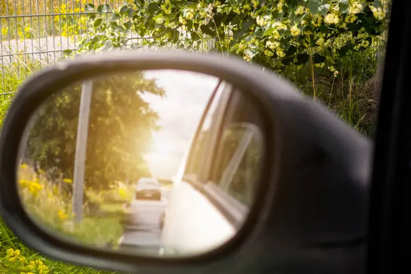 Bir araba yolda ilerliyor, ve dikiz aynasında, bir araba görülebilir. Araba çok uzakta..