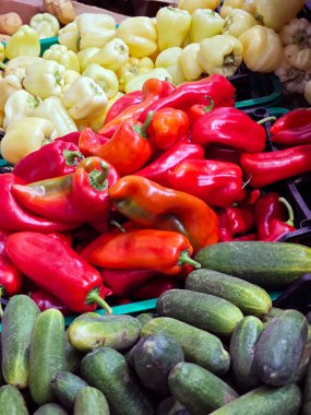 Parlak renkli dolgun çan biberleri ve salatalıklar kalabalık bir yerel pazarda sergilenerek gün ortasında taze ürünler sergileniyor. Satıcılar canlı sebzeli müşterileri cezbeder..