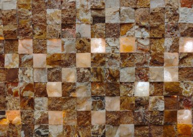 Üzerinde ışık parlayan kahverengi fayanslardan yapılmış bir duvar. Işık duvarda, fayansları aydınlatıyor ve sıcak, davetkar bir atmosfer yaratıyor. Fayanslar kareli desende dizilmiş.