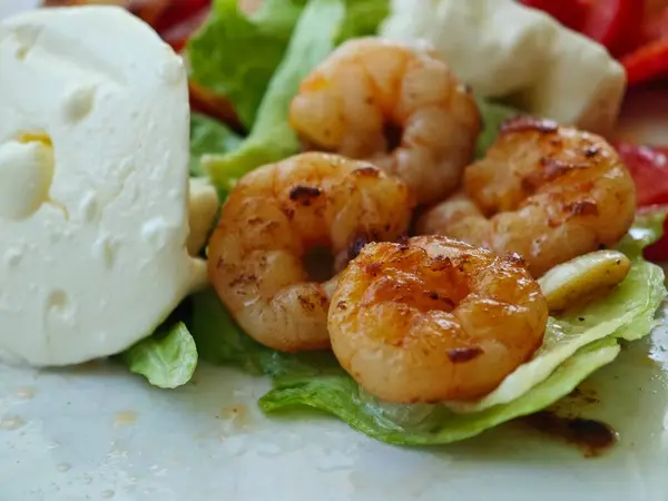 Yağda kızartılmış karides, krem peynir ve renkli sebzelerin yanında gevrek maruldan bir yatakta düzenlenir. Doğal ışık yemeğin tazeliğini vurgular.