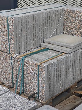 Sağlam beton levhalar ahşap bir paletin üzerine düzgünce istiflenmiş, kayışlar ve halatlarla güvence altına alınmış, hareketli bir şehir ortamında açık hava inşaat projeleri için kullanılmayı bekliyor..