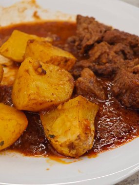 Tabakta, her ikisi de domates bazlı zengin bir sosa batırılmış ve sıcak bir restoran ortamında servis edilen kızarmış patateslerin yanında taze ızgara et yer alıyor..