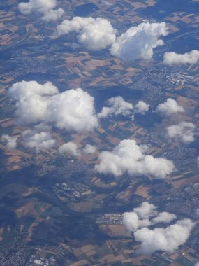 Hava görüntüsü dağınık beyaz bulutların tarlaların ve küçük kasabaların üzerinde yüzdüğünü gösteriyor. Manzara, açık mavi gökyüzünün altında yeşilin ve kahverenginin değişik tonlarına sahiptir..