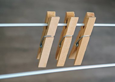 Yatay bir kabloya bağlanmış üç tahta mandalın yakın plan fotoğrafı, nötr bir arka plan içeriyor, günlük ev işleri ve tasarım basitliğini vurguluyor.