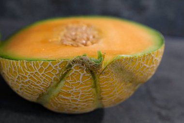 Taze kavun, koyu bir yüzeyde yarıya bölünür. Ortasında çekirdekler ve belirgin yeşilimsi sarı kabuklu canlı turuncu et sergilenir..