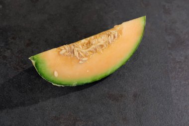 Bir dilim sulu kavun parlak turuncu derisini ve pürüzsüz koyu bir yüzeyde dinlenen yeşil kabuğunu ortaya çıkarır. Tohumlar görünür, meyvenin tazeliğini vurgular..