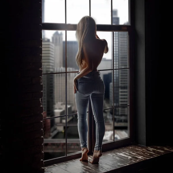 穿着牛仔裤的年轻貌美的女子站在窗边 观光城 — 图库照片