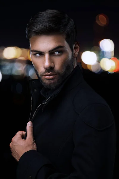 在一座夜城的背景下 一个穿着黑色外套和黑色衬衫 发型时髦的英俊的性男人的肖像 图库图片