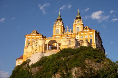 Avusturya 'daki Melk Abbey kalesi, gün batımında büyük turuncu barok bir bina.