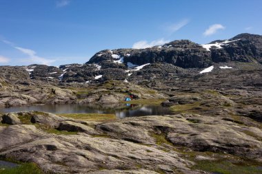 Norveç, Trolltunga 'ya giden temiz su gölü manzaralı, tanınmayan insanlar çadır kuruyor.