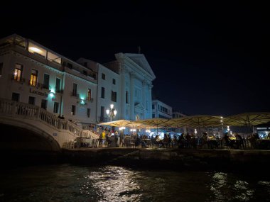 VENICE, İtalya - 1 Kasım 2024: Chiesa della Pieta - Santa Maria della Visitazione Kilisesi Venedik, İtalya 'da geceleri, insanlarla dolu bir restoran