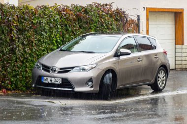 TOKAJ, HUNGARY - 27 Ekim 2023: Kahverengi Toyota Auris E180 model hatchback hibrid araba yağmur altında caddeye park edilmiş.