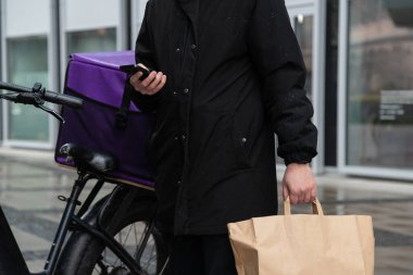 Bisikletli bir kuryedeki kurye telefonundaki haritaya bakar ve sipariş vermek için adres arar.