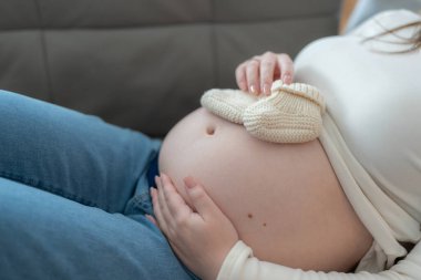 Karnında bebek ayakkabıları taşıyan hamile bir kadın evinde koltukta dinleniyor. Yüksek kalite fotoğraf