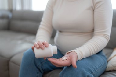 Elinde haplarla plastik kavanoz tutan hamile bir kadın. Kanepede otururken vitamin ve mineral tedavisi görüyor. Yüksek kalite fotoğraf