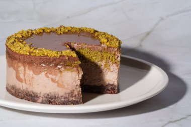 Fıstık ezmeli Dubai çikolatalı cheesecake ve beyaz tabakta çikolata ganache ile kaplanmış kataifi hamur. Kopyalama alanı olan beyaz arkaplan. Hoşgörü, gurme tatlılar, aşçılık sanatı.