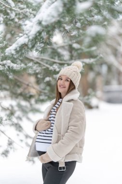 Karlı bir kış ormanında neşeli, hamile bir kadın. Annemin gülümsemesini ve karnını dışarıda tutmasını bekliyorum. Annelik kavramı, aşk, bekleyiş ve hamileliğin doğayla iç içe olması.