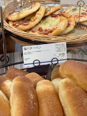 Kyoto, Japan - May 25, 2024: Freshly baked salted butter rolls and mini pizzas on display in Japanese bakery. Concept of bakery delights, Japanese cuisine, and appetizing comfort food. High quality