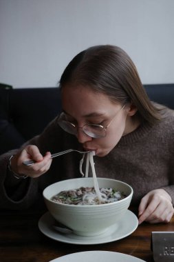 Geleneksel Vietnam pipo çorbası içen genç bir kadın biftek ve erişteli. Otantik Asya mutfağından, konforlu yiyeceklerden ve kültürel yemek deneyiminden zevk alma kavramı. Yüksek kalite fotoğraf