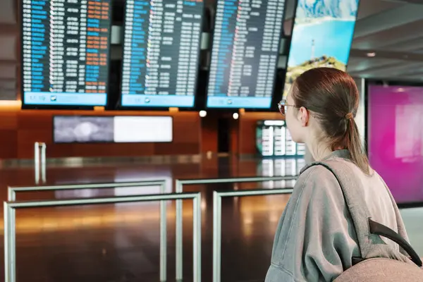 Genç bir bayan yolcu, havaalanının kalkış panosunu sırt çantasıyla kontrol ediyor. Seyahat planlama ve seyahat beklentisi kavramı. Yüksek kalite fotoğraf