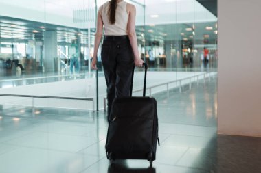 Havaalanı terminalinde bavuluyla yürüyen genç bir kadın. Bağımsız seyahat kavramı, modern yaşam tarzı ve kusursuz hareket kabiliyeti. Fotoğraf hareket halinde, yumuşak odaklanma